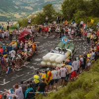 photo prise sur l'étape 11 du tour de france 2024 : la voiture en forme de poireau de E.Leclerc est saluée par la foule. Derrière vient la moto en for