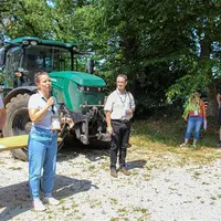 Des agriculteurs et experts debout devant un tracteur vert.