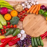 Plusieurs fruits et légumes posés sur une table en bois, incluant des tomates, carottes, courgettes, poivrons, de l'ail,