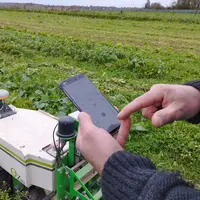 Le robot OZ de Naïo dans un champs. Un maraîcher dont on voit seulement les bras pianote sur l'application liée au robot.