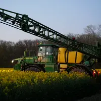 Pulvérisateur effectuant des traitements phytosanitaires le soir dans un champ de colza.