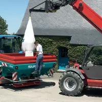 Agriculteur déchargeant un sac d'engrais dans son épandeur à engrais.