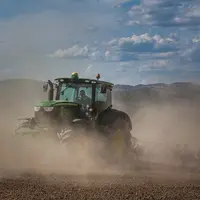 Tracteur entouré d'un nuage de poussières dans une parcelle de sol nu.