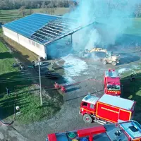 Vue de drone de l'incendie d'un bâtiment agricole recouvert de panneaux photovoltaïques avec camion de pompiers