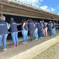 Agricultrices de dos devant une étable avec des gilets floqués au nom La Cavac