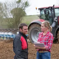 Un agriculteur et sa conseillère bancaire devant le tracteur dans un champ