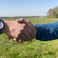 Deux personnes se serrent la main dans un champ.