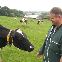 Eleveur laitier souriant avec une vache dans une prairie