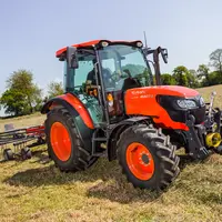 Tracteur agricole Kubota M4073 avec un andaineur au travail