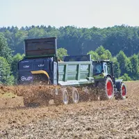 Epandeur à fumier Fliegl KDS 255 Muck Control derrière un tracteur Claas en action.