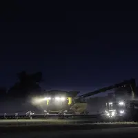 Moissonneuse-batteuse CR 11 New Holland battant de nuit, accompagnée d'un tracteur New Holland et d'une benne