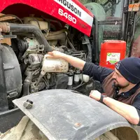 Opérateur qui réalise l'appoint d'huile dans le moteur du tracteur.