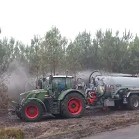 Tracteur et tonne à lisier arrosant la lisière d'une forêt.