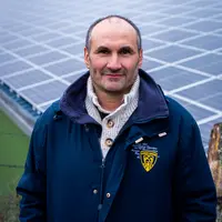 Un agriculteur devant un hangar dont la toiture est couverte de panneaux photovoltaïques.