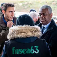 Trois personnes parlent, l'une d'elle est de dos et porte un gilet flanqué FNSEA 63.