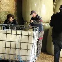 Deux personnes nouent des ficelles dans un récupérateur d'eau, filmés par un troisième