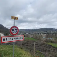 un panneau avec écrit 50 et Neussargues, en arrière plan le village