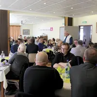 Une personne, debout, parle, un groupe assis à table l'écoute.
