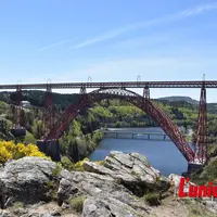 Un rocher avec des fleurs jaunes et derrière le viaduc rouge.