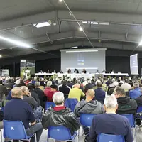 Le public, assis sur des chaises plastiques, écoute les explications à la tribune lors de l'assemblée générale des chasseurs de Lozère