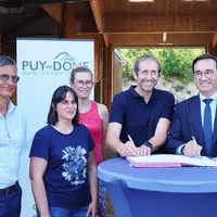 trois hommes et deux femmes souriants signent un contrat devant un panneaux du puy-de-dôme
