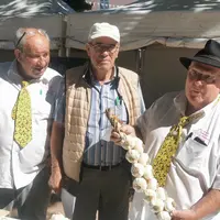 Trois hommes âgés, l'un deux tient une tresse d'ail