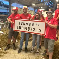Un groupe de gens tient un panneau signalétique de commune à l'envers dans une étable paillée