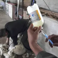 une seringue charger avec un liquide avec un mouton en train d'être tondu en arrière-plan
