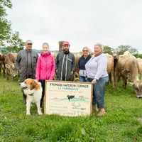 Une famille tenant un panneau devant un troupeau de vache dans la campagne