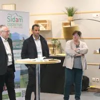 Quatre personne debout devant un kakémono sidam-copamac, l'un d'entre eux parle dans un micro