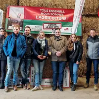 Un groupe d'agriculteurs pose devant des ballots de paille dans un grange de montagne.