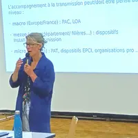 Une femme à lunettes tenant un micro devant un écran de projection