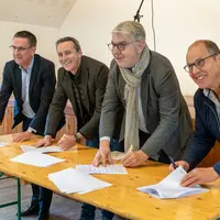 Quatre hommes souriants signent un contrat sur une table.