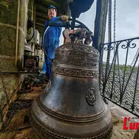 Dans un clocher, un campanaire pose fièrement devant une cloche fraîchement restaurée.