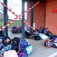 Une entrée d'école fermée par de la rubalise et des cartables restés devant, sans enfant.