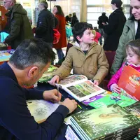 Un dessinateur en train de dédicacer une bande-dessinée à deux enfants et leur maman