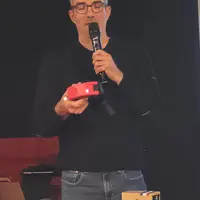 un homme parle dans un micro, un collier anti-loup à la main