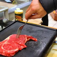 une pièce de boeuf sur une plancha, prête à être retournée à la fourchette