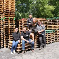 Cinq personnes posant devant des piles de palettes en bois.