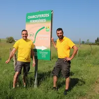 Deux hommes devant un panneau de promotion d'une exploitation agricole.