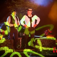Deux personnages en costume du début du XXe siècle encerclés de lumières.