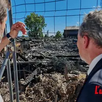 deux hommes de dos observent derrière des grilles un bâtiment calciné.