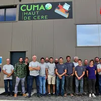 un groupe d'agriculteurs devant le pignon d'un bâtiment agricole avec le logo d'une Cuma