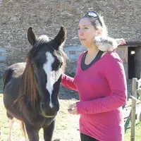 Une dame, à côté d'un cheval et avec un coq sur les épaules