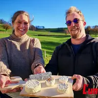 Un couple présente un plateau de fromages de chèvres, dans un paysage de campagne