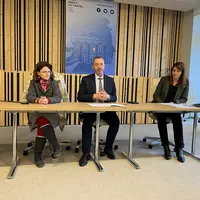 Trois personnes présentent un bilan à une table dans une salle de préfecture