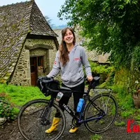 Jeune femme en bottes jaunes, dans un cadre champêtre, tient un vélo.