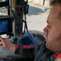 agriculteur dans la cabine de son tracteur pilote l'autoguidage sur un écran tactile.