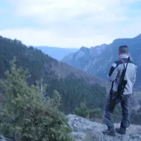 Un chasseur observe une vallée un fusil sur l'épaule.