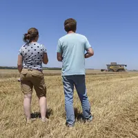 Un agriculteur et sa fille dans un champ avec moissonneuse batteuse au loin.